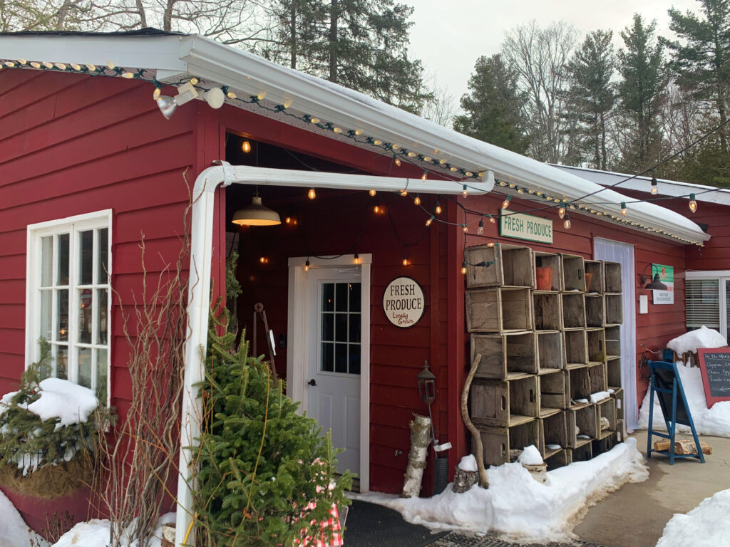 Side entrance of red barn pictured with fresh produce sign and lights