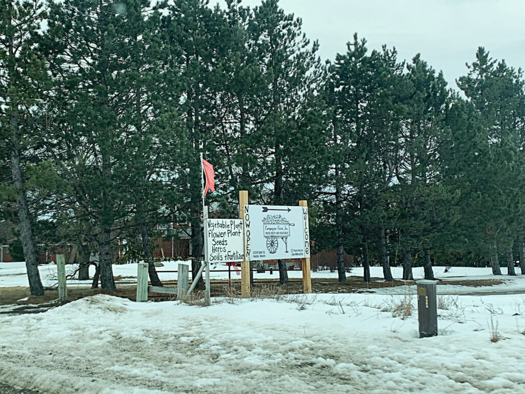 White standing sign in front of trees advertises produce