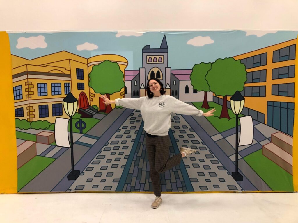 Woman posing in front of a mural of a school campus.