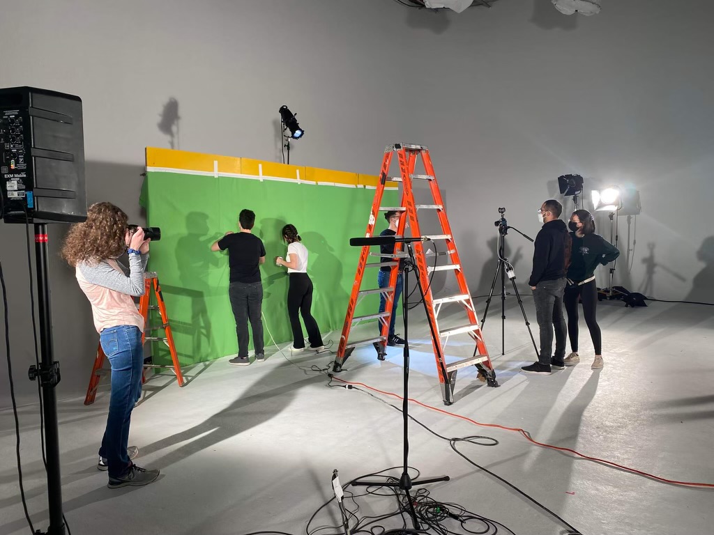 People filming a man and woman acting in front of a green screen.