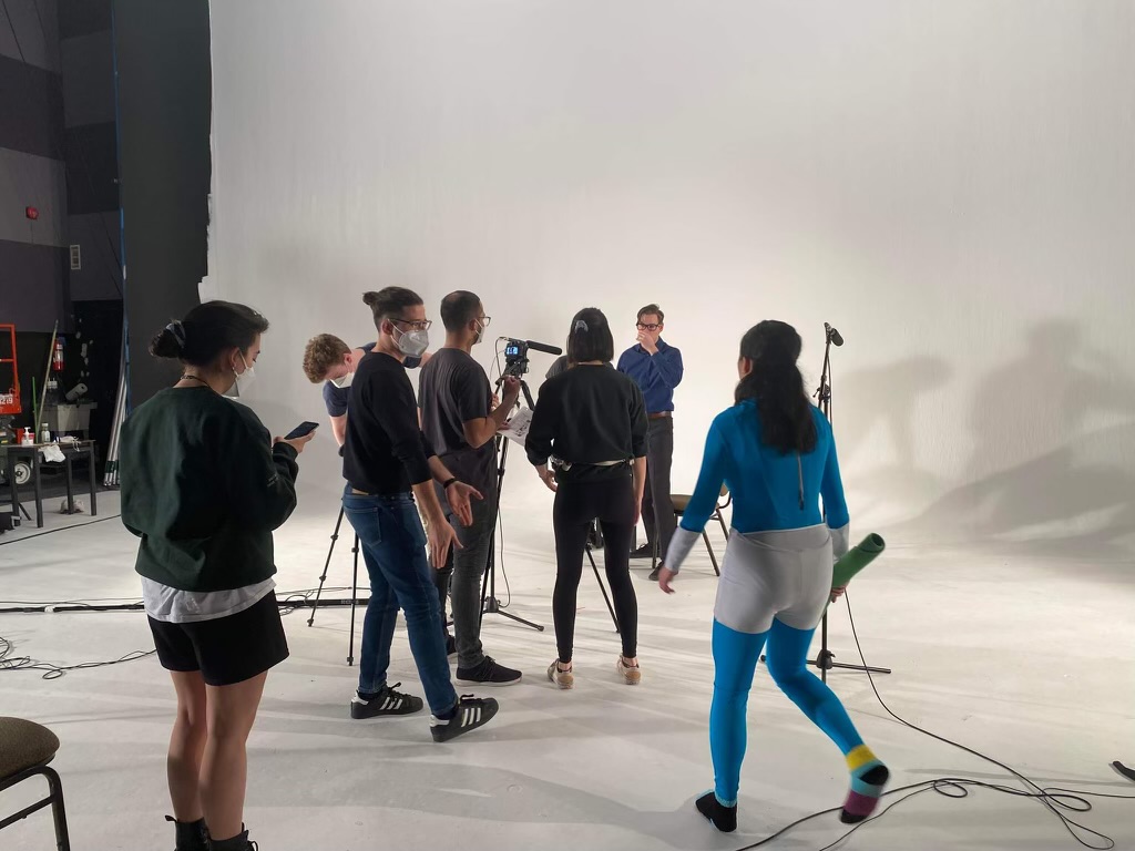 People inside a filming studio walking around and looking at a camera.