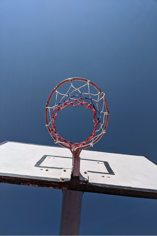 A view of a basketball rim from underneath. Blue sky all around it.